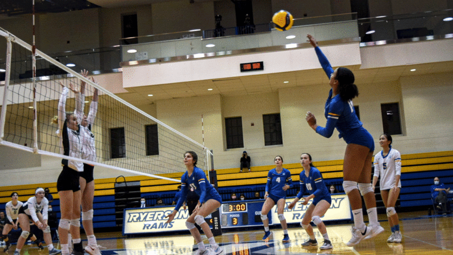 A Rams women's volleyball player in a blue jersey spikes the ball