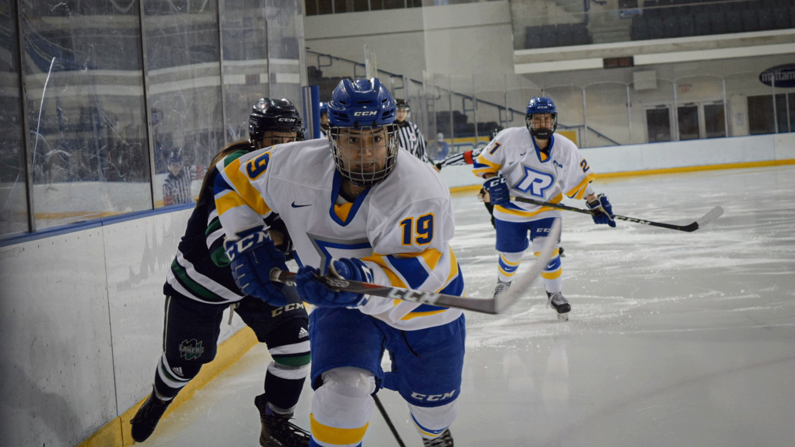 A Rams women's hockey player in a white jersey chases the puck