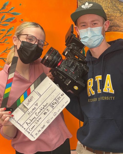 Audrey Crunkleton on the left, and Chris Van Haren on the right holding a slate and a camera in front of an orange background.