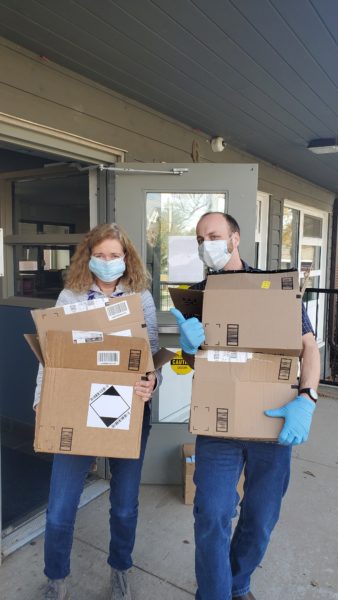 YWS’s Development Administrator, Heather McGowan and Community Engagement and Education Specialist, Mike Burnett standing in front of an open door holding a stack of cardboard boxes with blue gloves on.