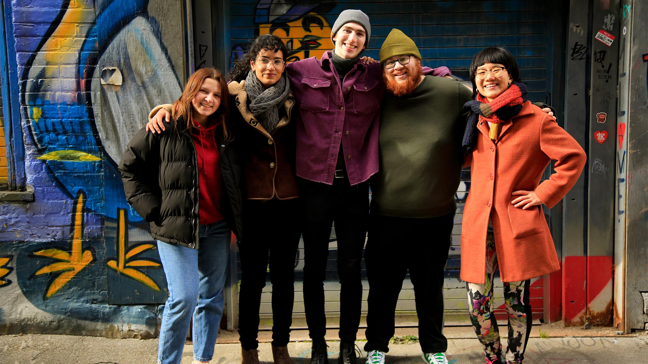 from left to right volunteers Sheridan Riggillo , Sofia Nemecek, Colwyn Alletson, Ethan Goldberg , Vicky Wang standing together in front of a graffiti wall