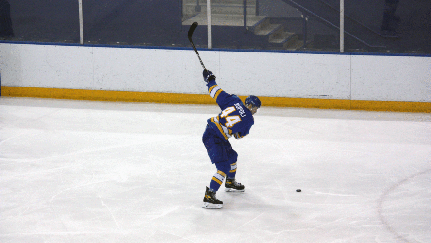 A Rams men's hockey forward in a blue jersey shoots the puck