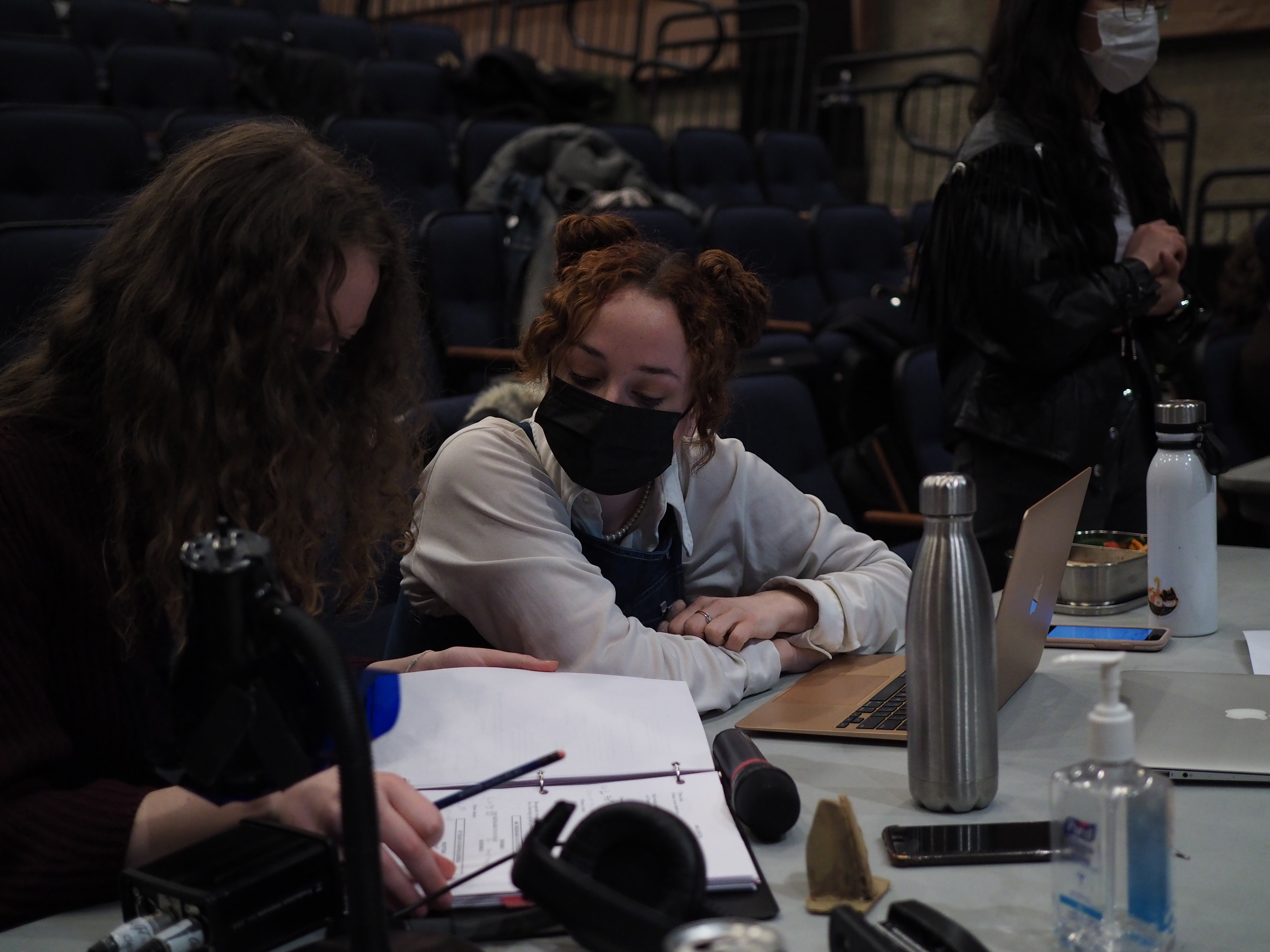 Two people looking at a binder and a laptop at a table in front of the stage.