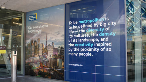 Sign in front of the SLC defining what it means to be metropolitan. The text says "To be metropolitan is to be defined by big city life—the diversity of its culture, the density of its landscape, and the creativity inspired by the proximity of so many people."