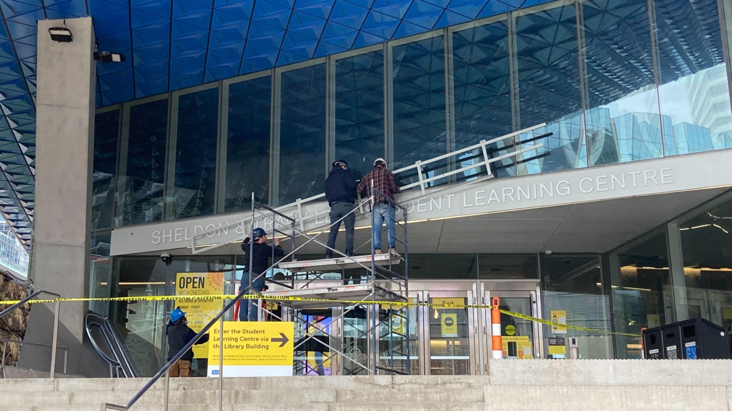 Four men in front of the SLC removing "Ryerson" from signage