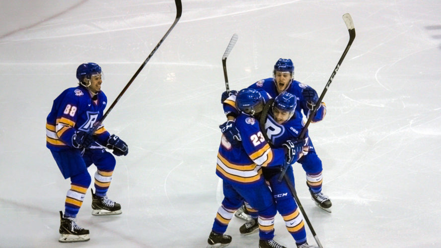 A group of hockey players in blue jerseys celebrate a goal