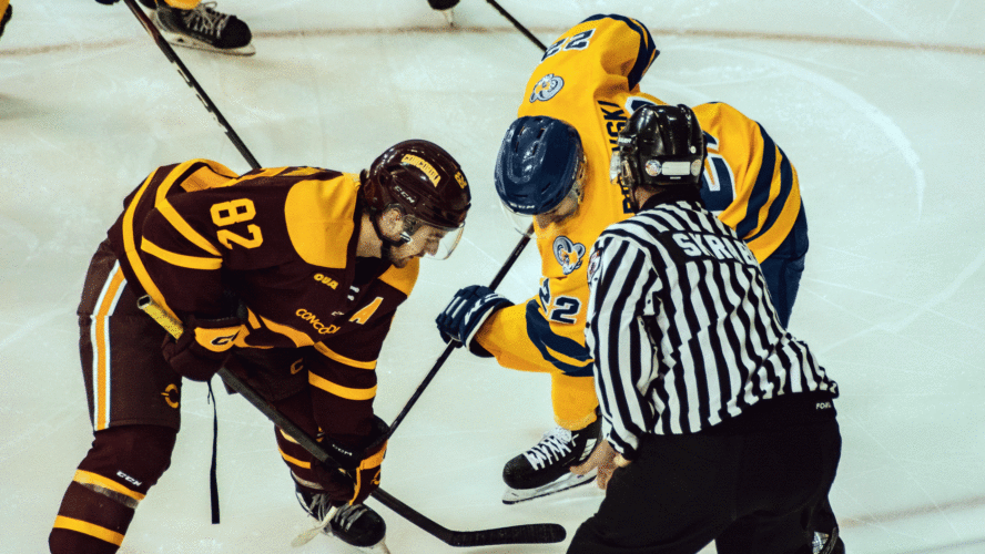 A hockey player in a yellow jersey and a hockey player in a burgundy line up for a draw