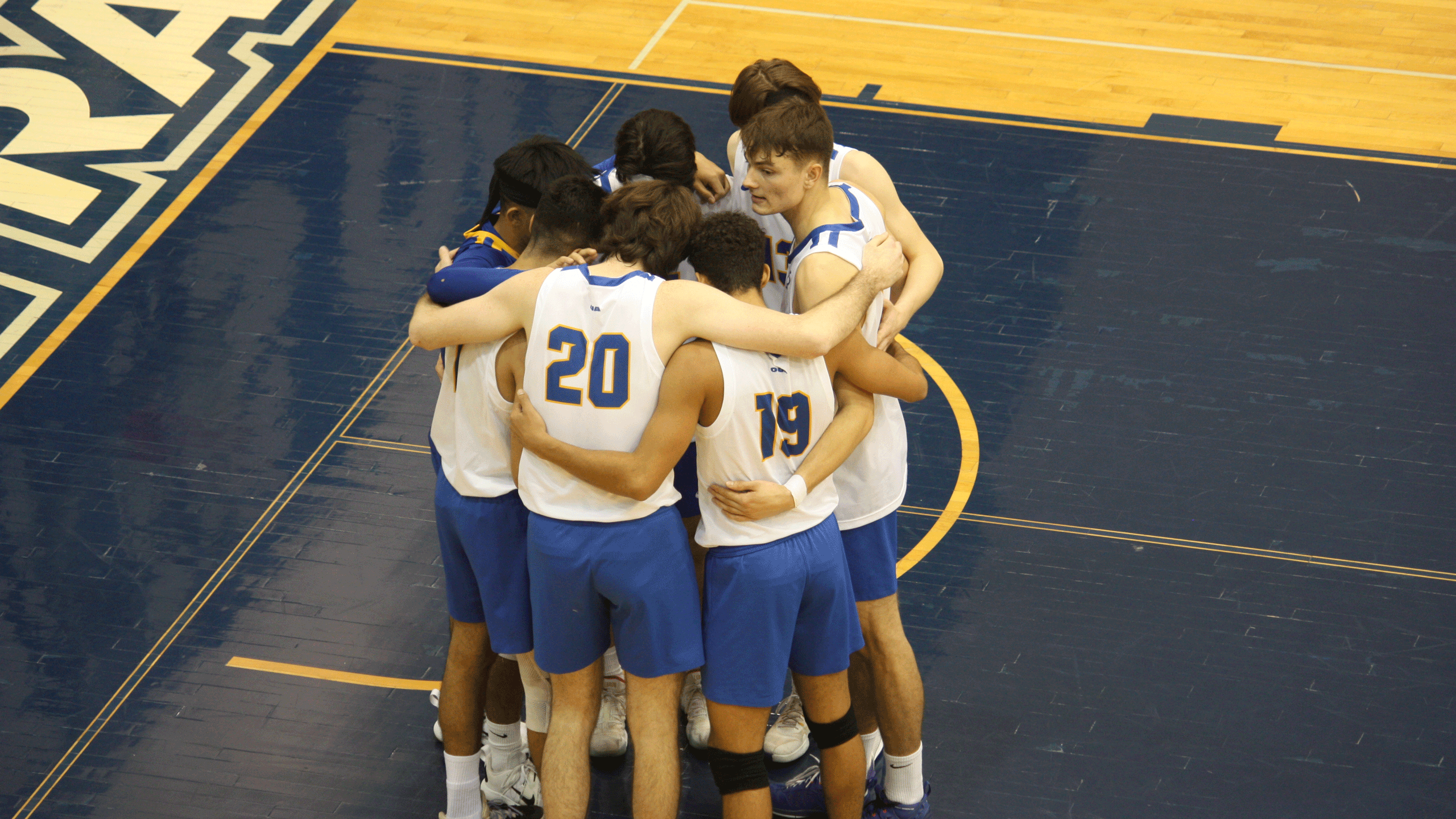 A group of volleyball players in white jerseys huddle