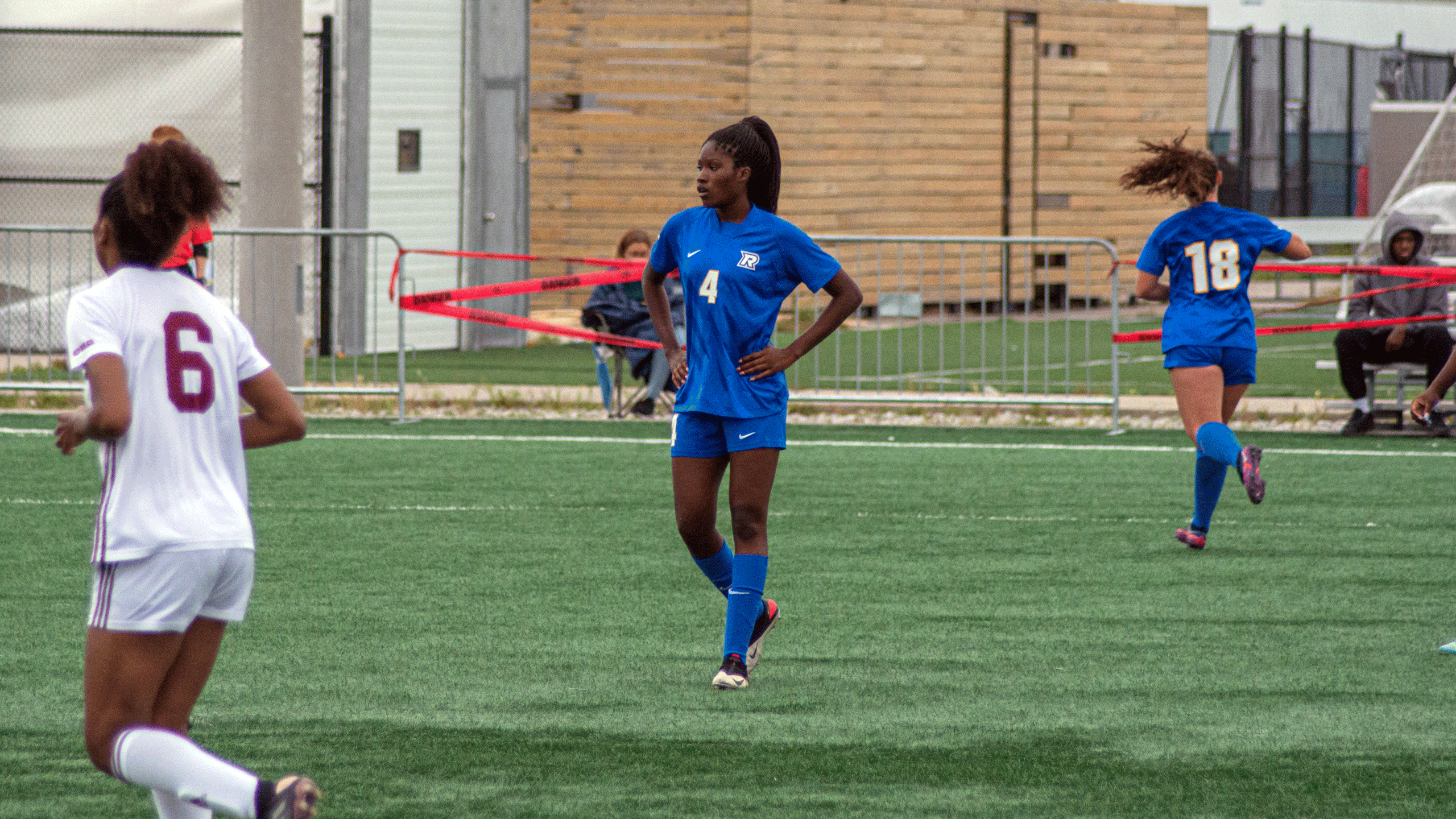 A TMU Bold women's soccer player in a blue jersey stands with their hands on their hips