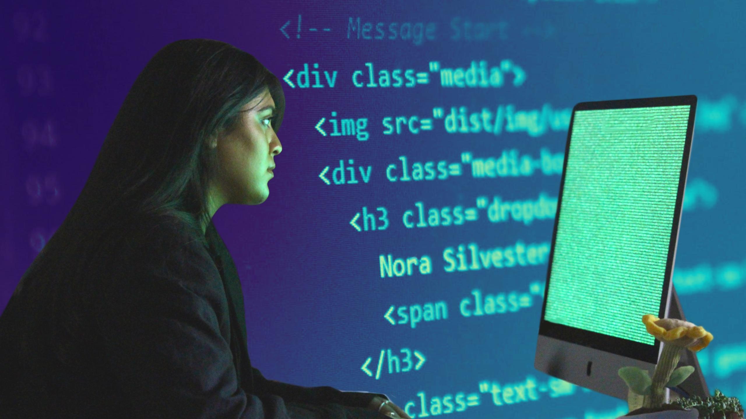in front of a green coding screen sits a woman staring into the screen
