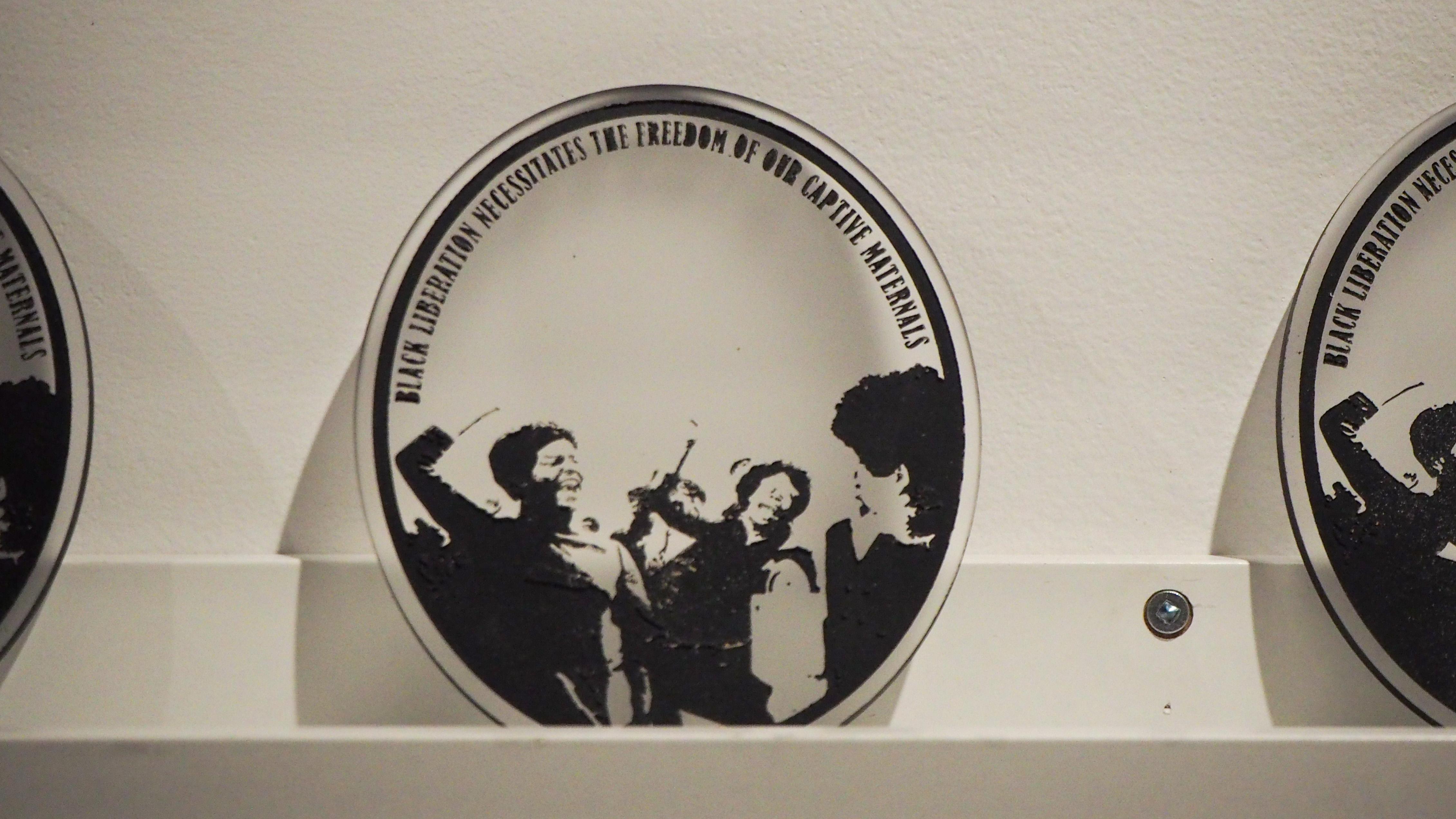 A medallion with a black-and-white photo of Black women and text that reads "Black liberation necessitates the freedom of our captive materials"