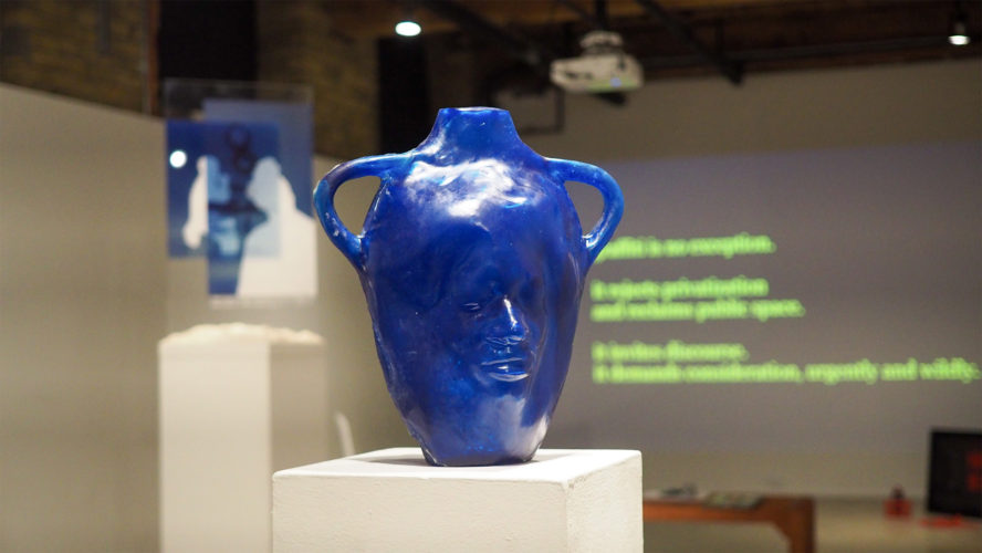 A blue pot in the middle of the gallery, sculpted with a face on it