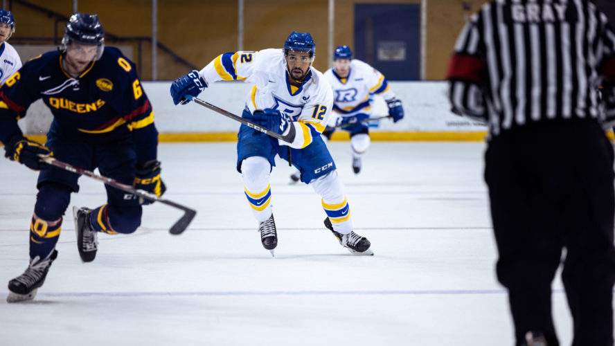 A TMU men's hockey player skates up the ice close to a Queen's player
