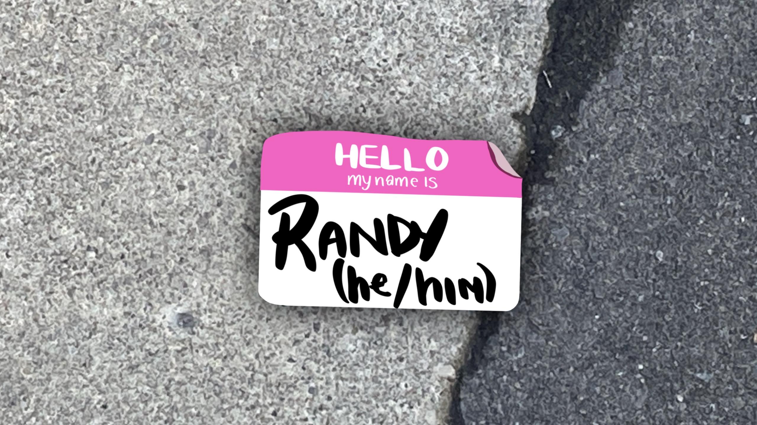 On pavement, an illustrated name tag saying "hello, my name is, randy he/him"