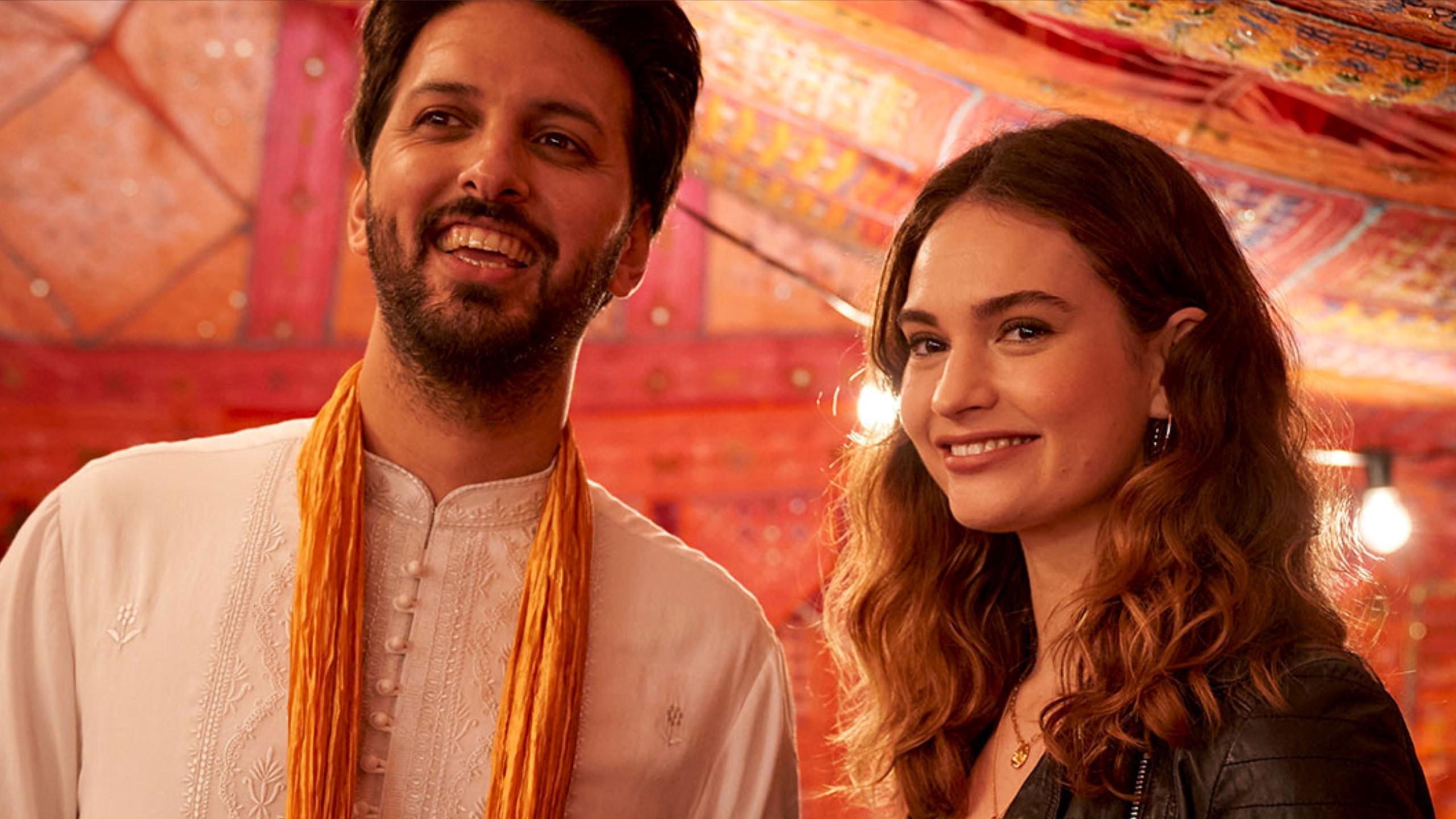 A man and woman stand ina colourful well lit room smiling at something behind the camera