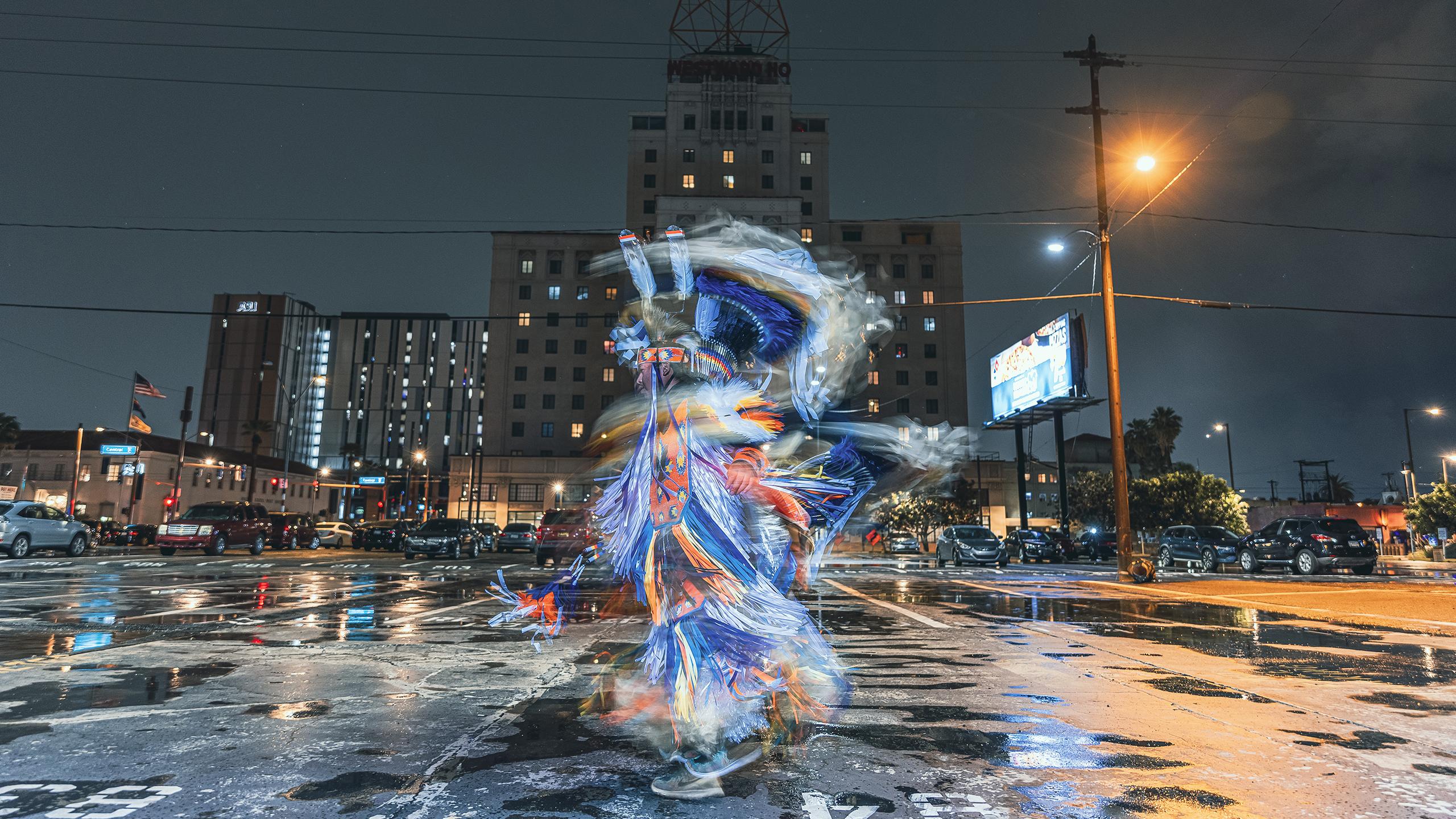 Photo of an Indigenous Enterprise dancer spinning in a rainy parking lot. 