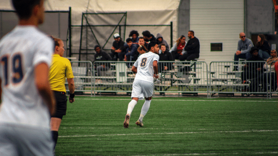 A TMU men's soccer player in white jersey runs up the field