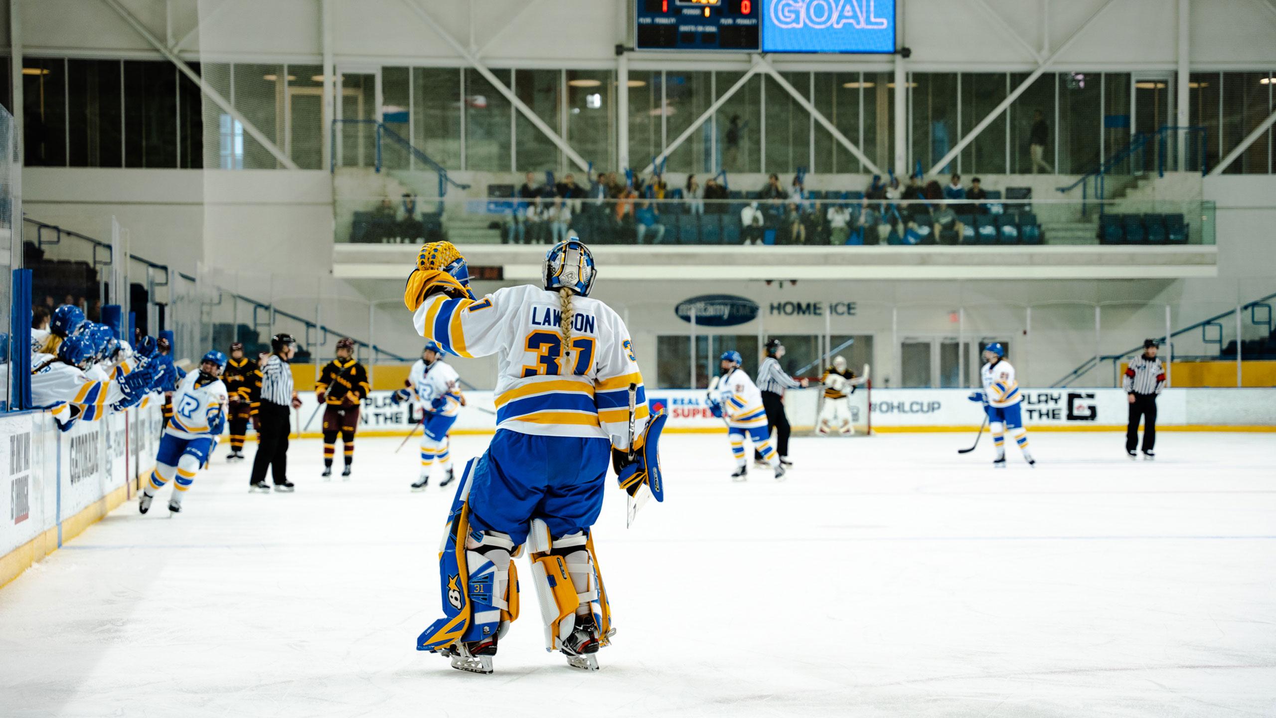 A TMU women's hockey goalie in a white jersey skates out of the net to high five teammates