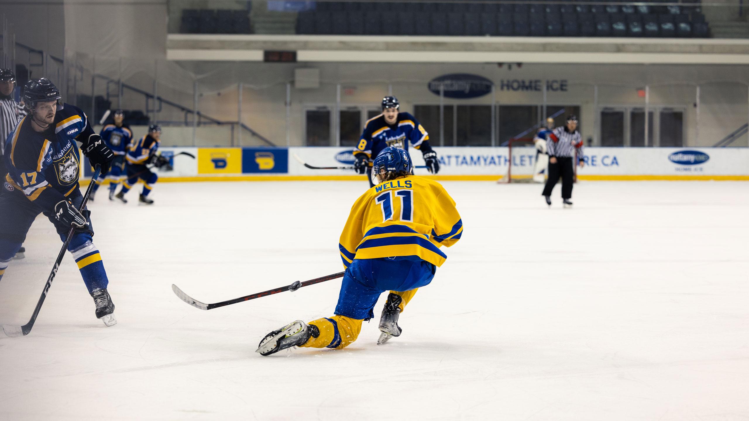 A TMU men's hockey player in a yellow jersey down on one knee blocking a shot