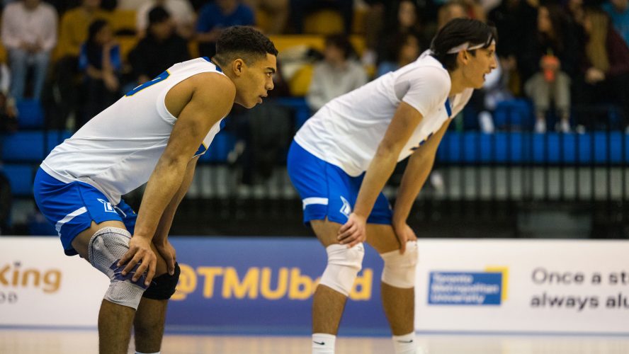 Two TMU men's volleyball players in white jerseys with their hands on their knees