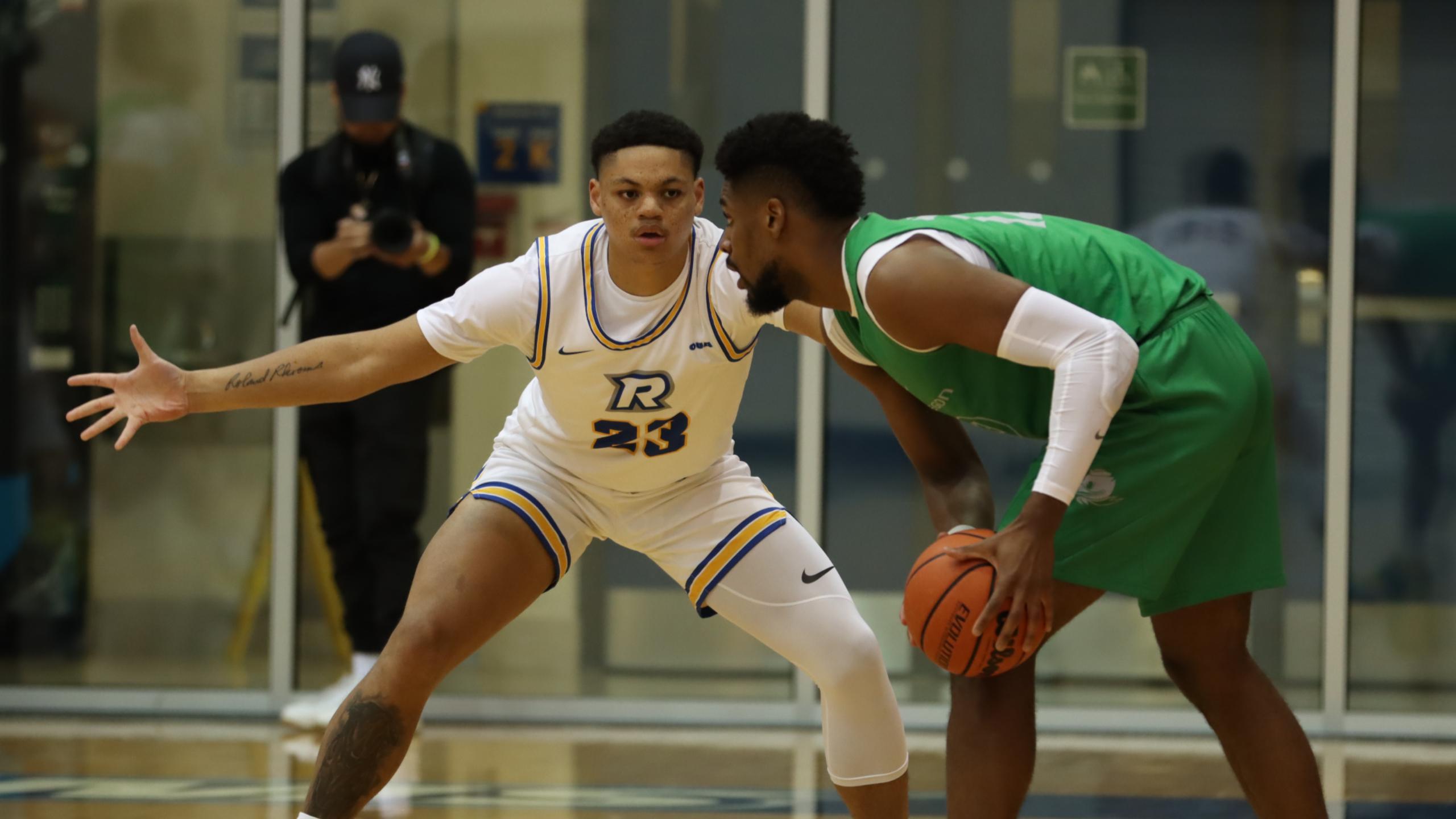 A TMU men's basketball player in a white jersey plays defence against an Oregon player in a green jersey