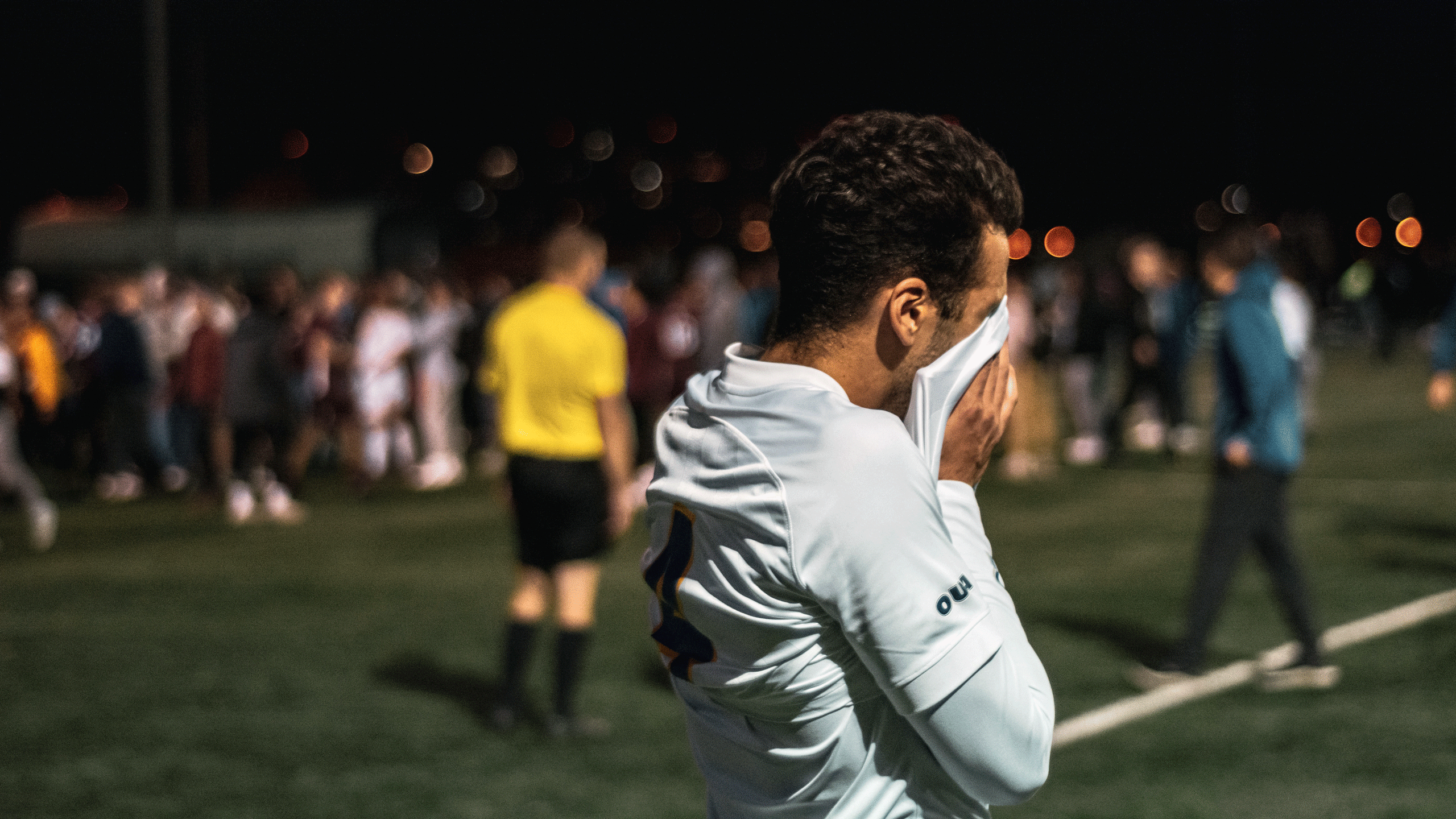 A men's soccer player in a white jersey puts his head in his jersey after a loss