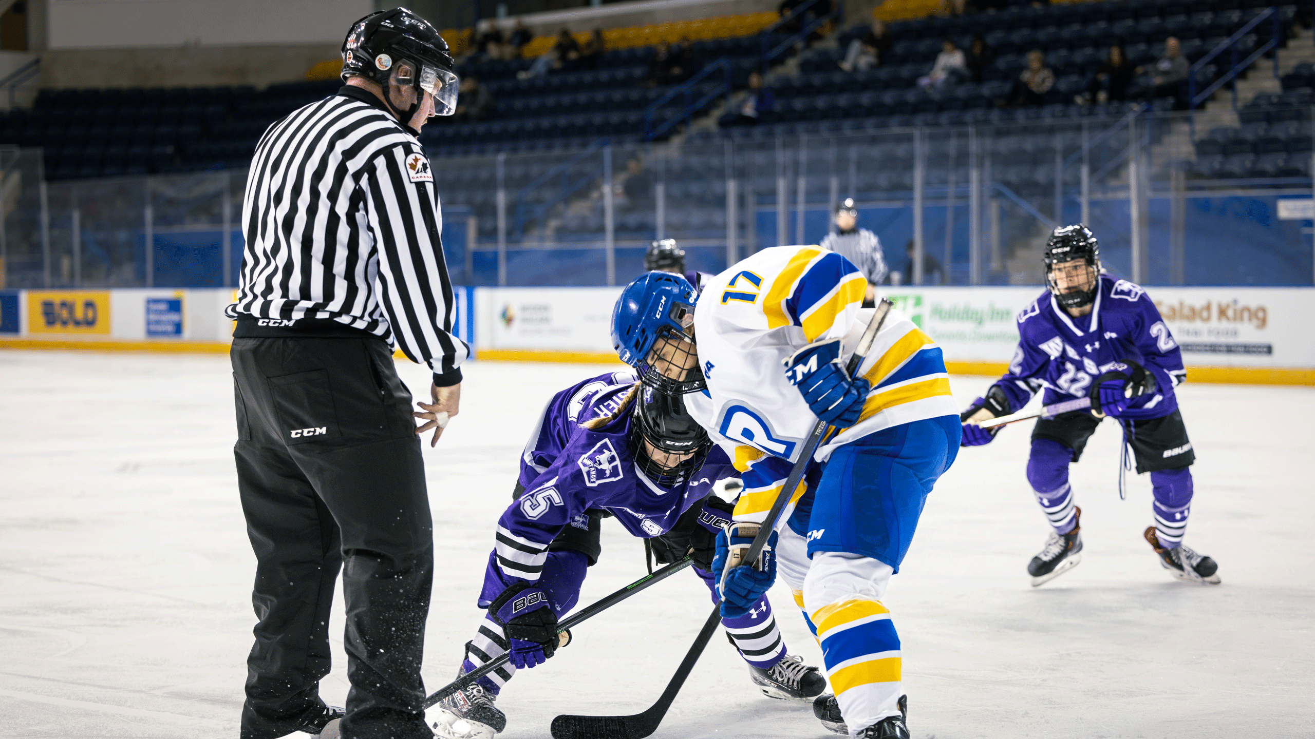 A hockey player in a white jersey battles with a player in a purple jersey