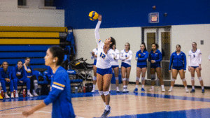 A TMU women's volleyball player in a white jersey serves the ball