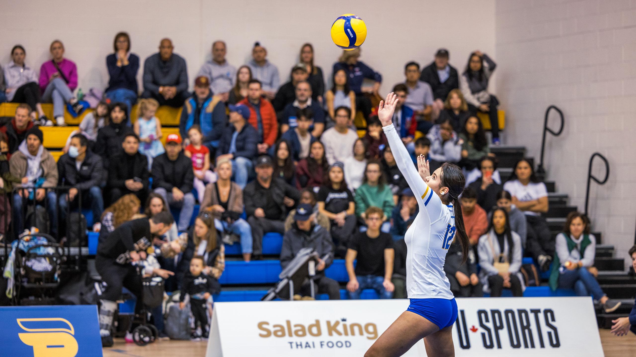 A TMU women's volleyball player in a white jersey serves the volleyball