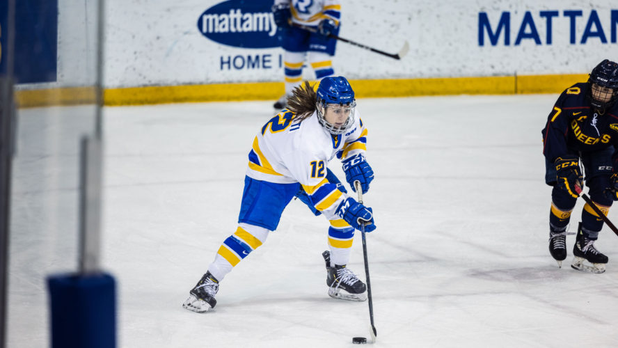 A TMU women's hockey player in a white jersey brings the puck up the ice