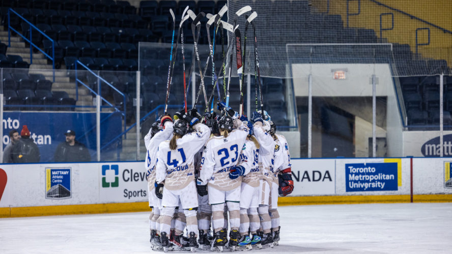 Members of Team World in white jerseys raise their hockey sticks to the sky during PHF all-star weekend