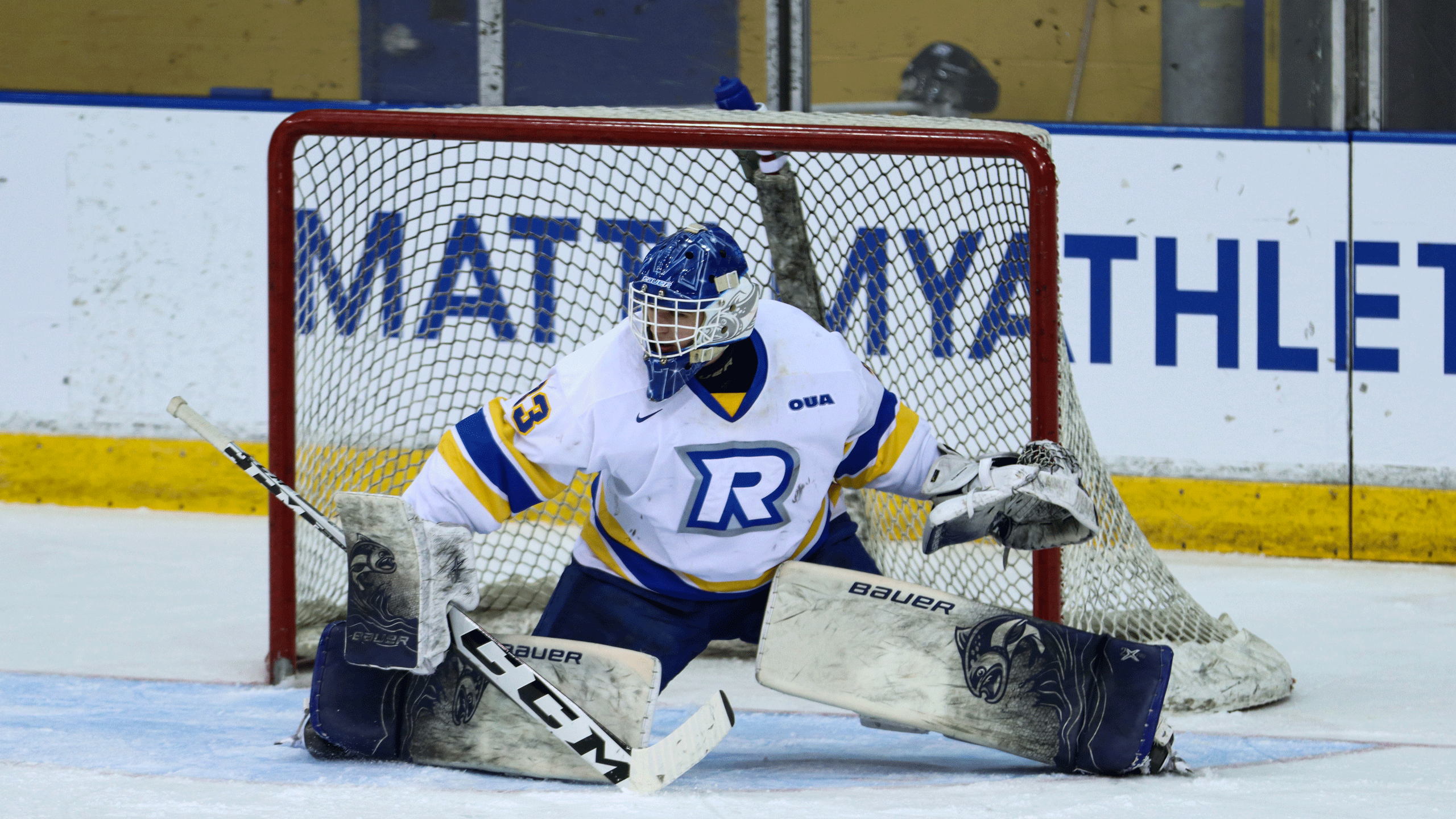 A hockey goalie in a white jersey skates across the ice