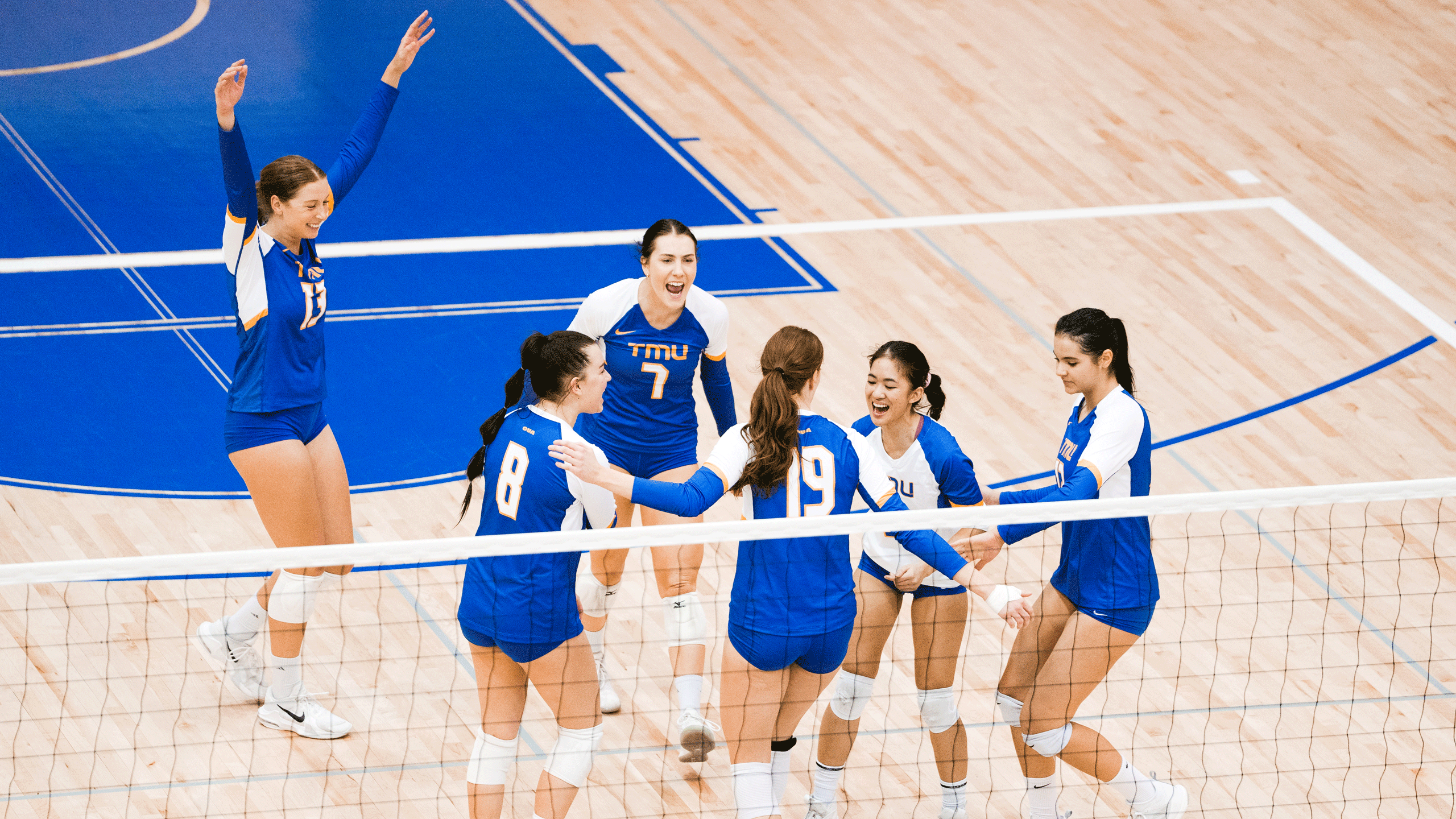 A group of volleyball players in blue jerseys celebrate