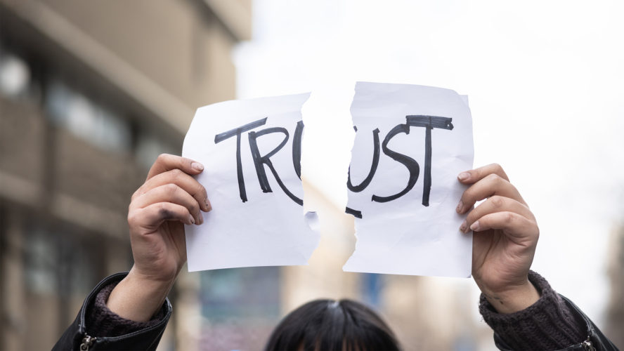 Women holding up a ripped paper with the word trust on it
