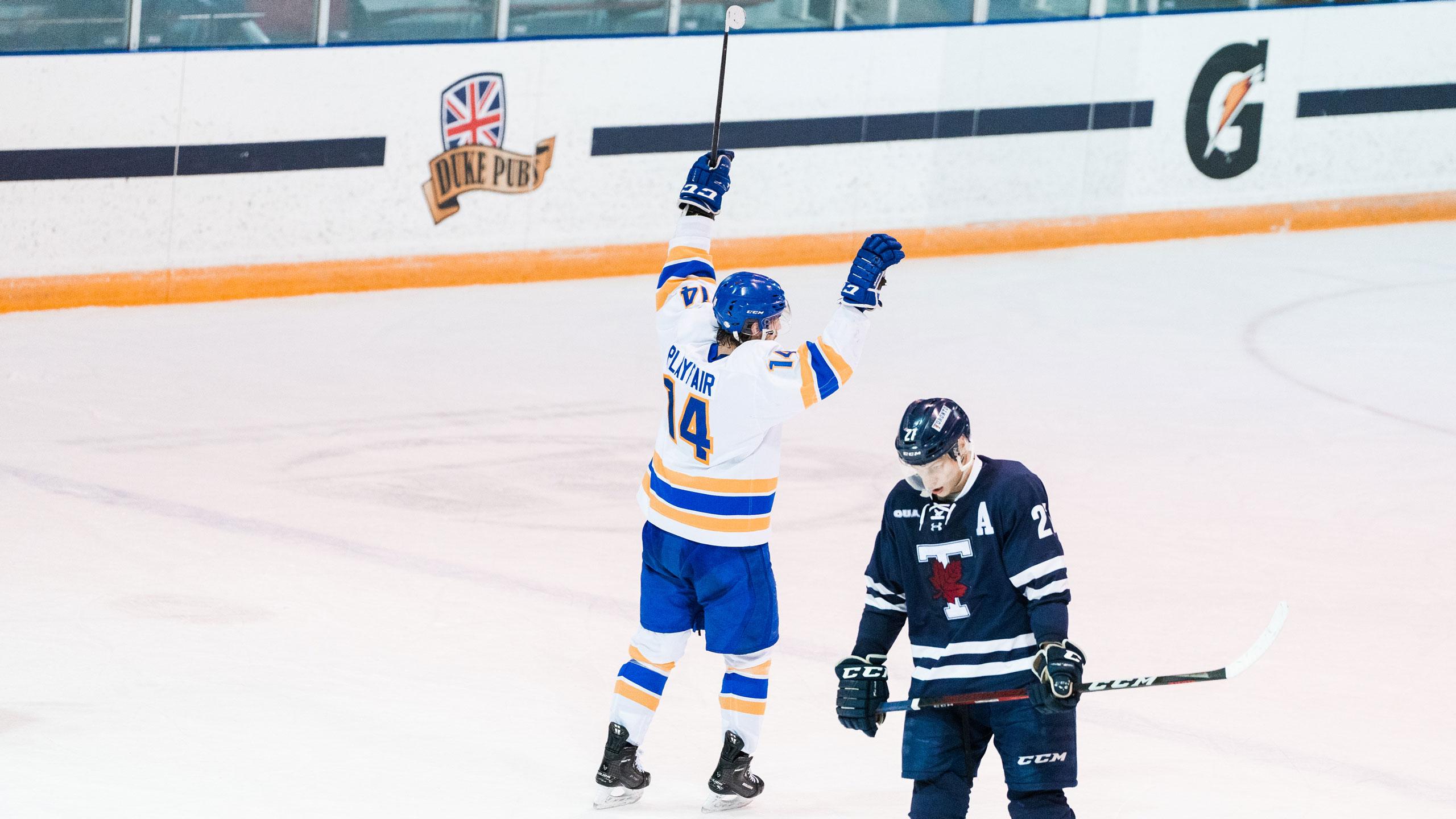 A TMU men's hockey player in a white jersey celebrates near a Varsity Blues player in a blue jersey