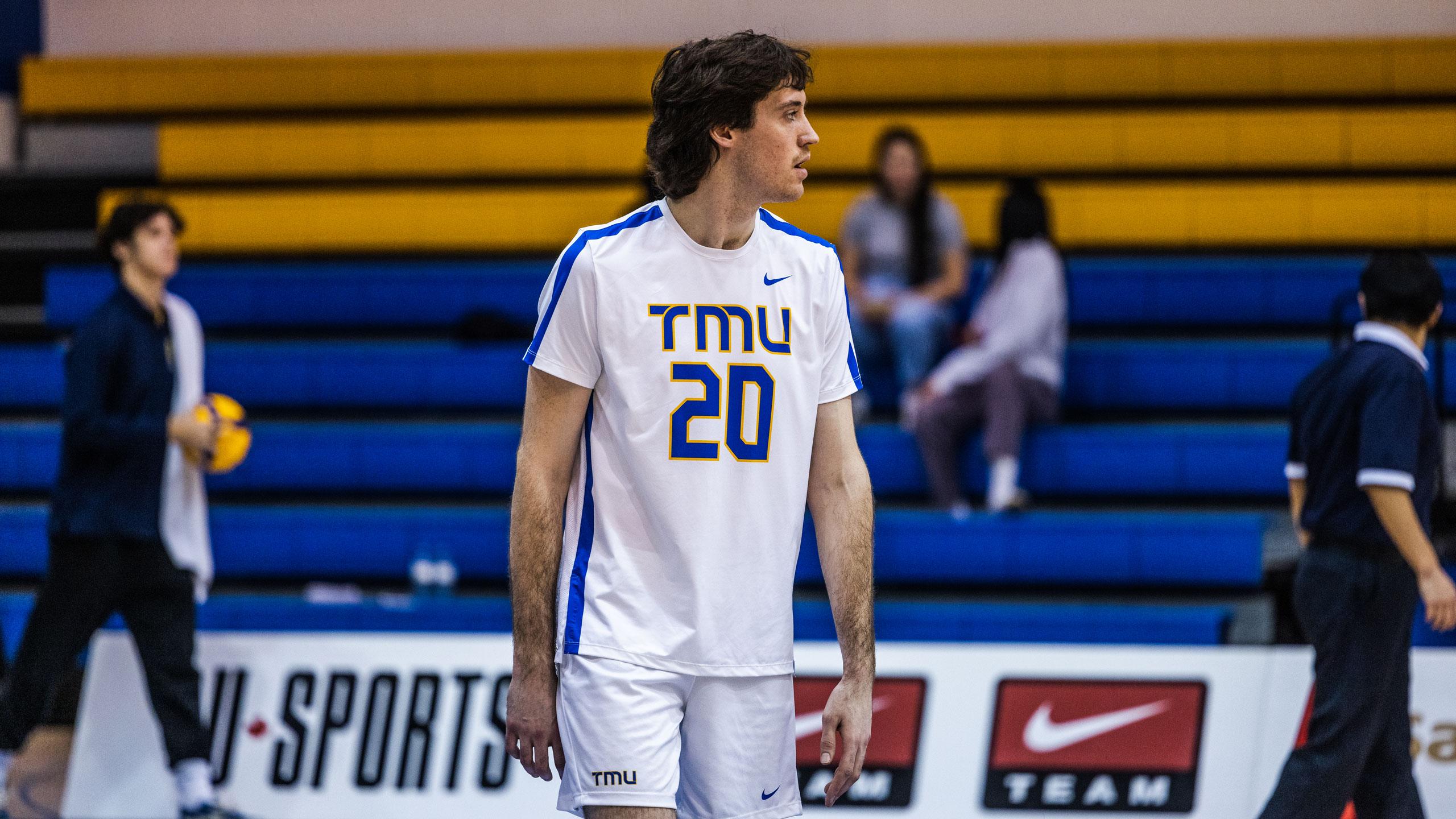 A TMU men's volleyball player in a white jersey looks towards the net
