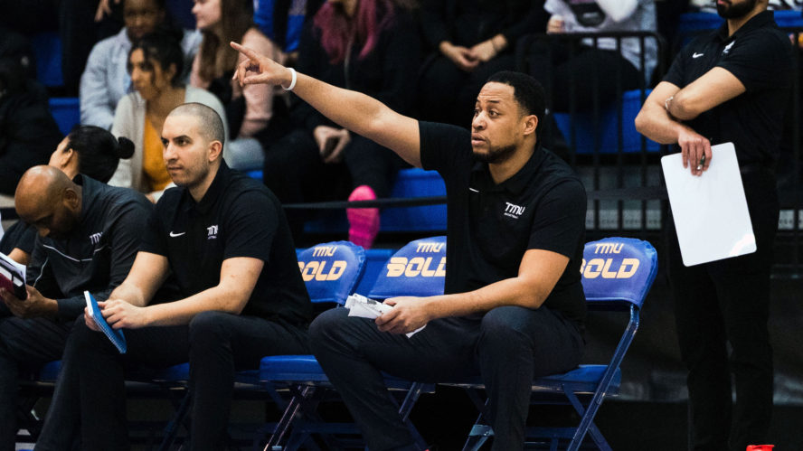 TMU men's basketball assistant coach Jeremie Kayeye points to the floor in a black shirt