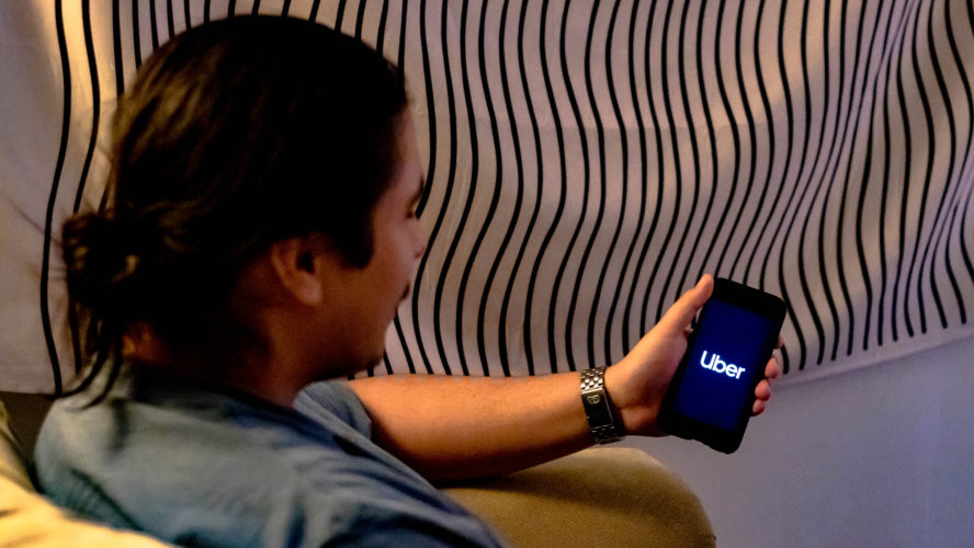 A man sits on a sofa using Uber on a phone