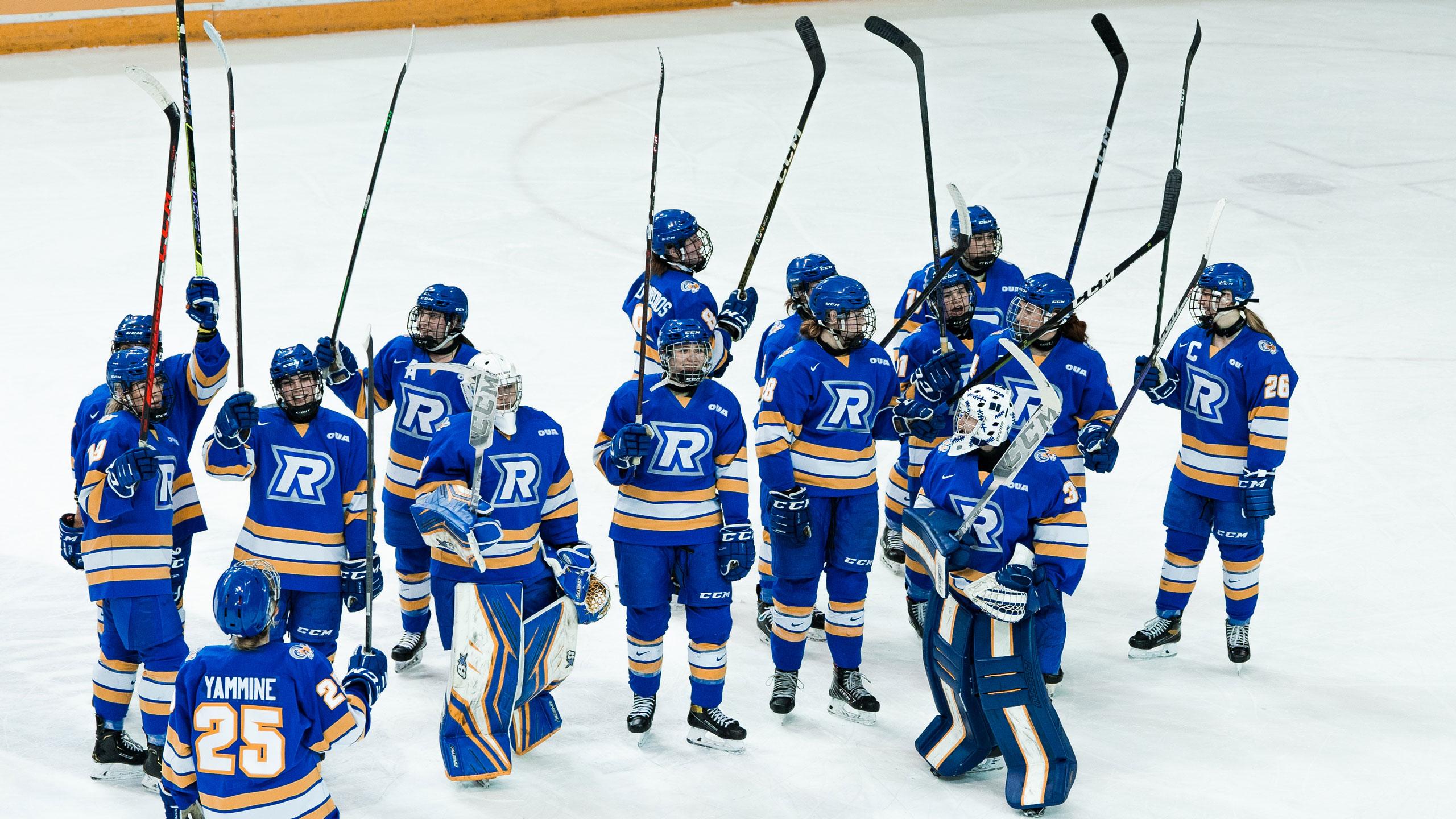 The TMU women's hockey players in blue jerseys stick their sticks in the air following a win