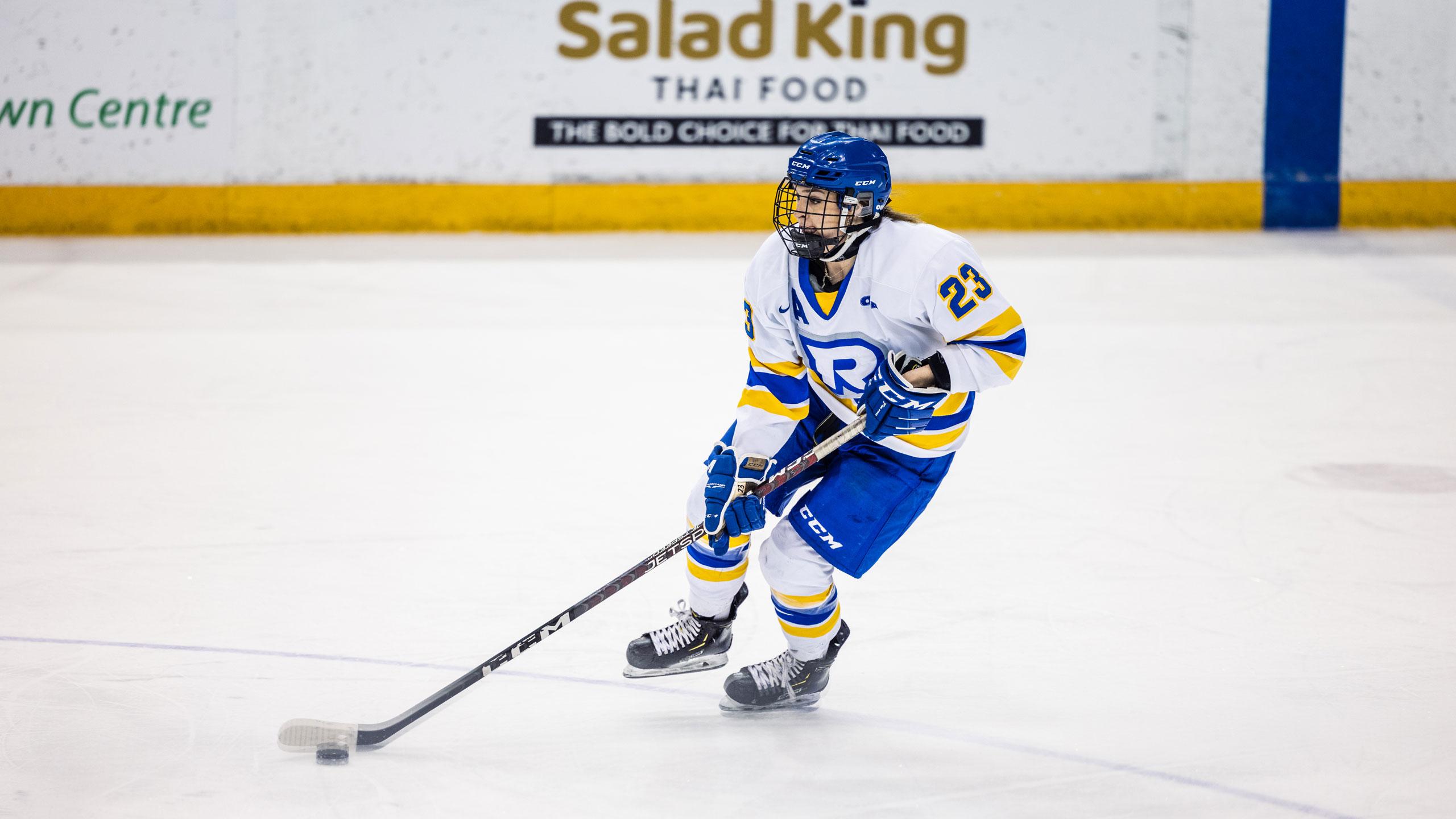 A TMU women's hockey player in a white jersey skates up the ice