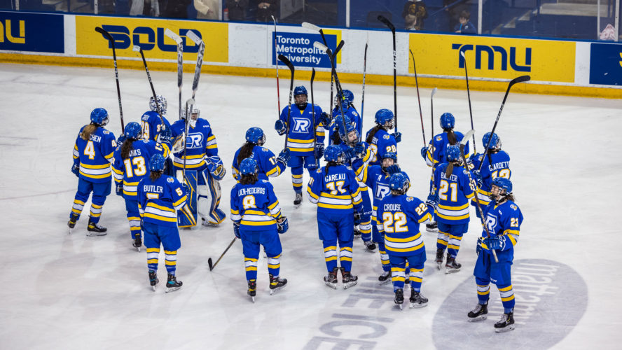 The TMU women's hockey team salutes the home crowd with their sticks in blue jerseys