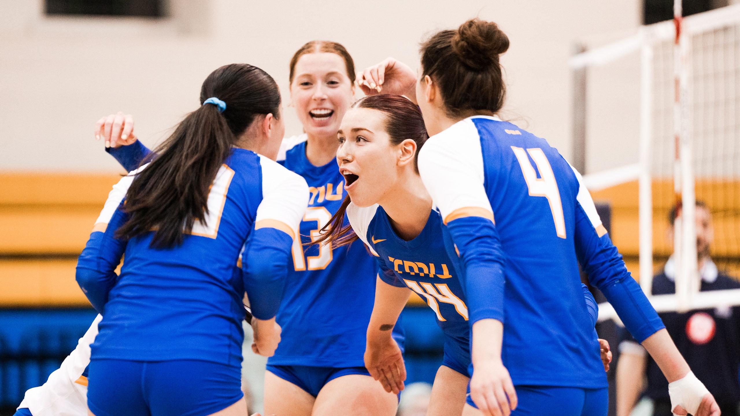 TMU women's volleyball players in blue jerseys celebrate a point