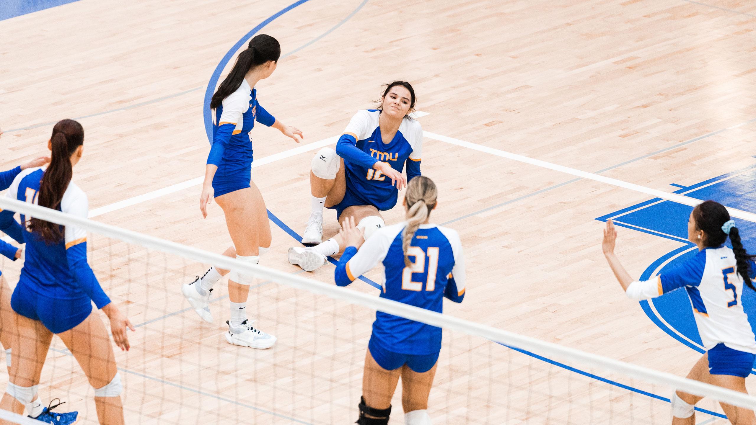The TMU women's volleyball team helps up their teammate in blue jerseys