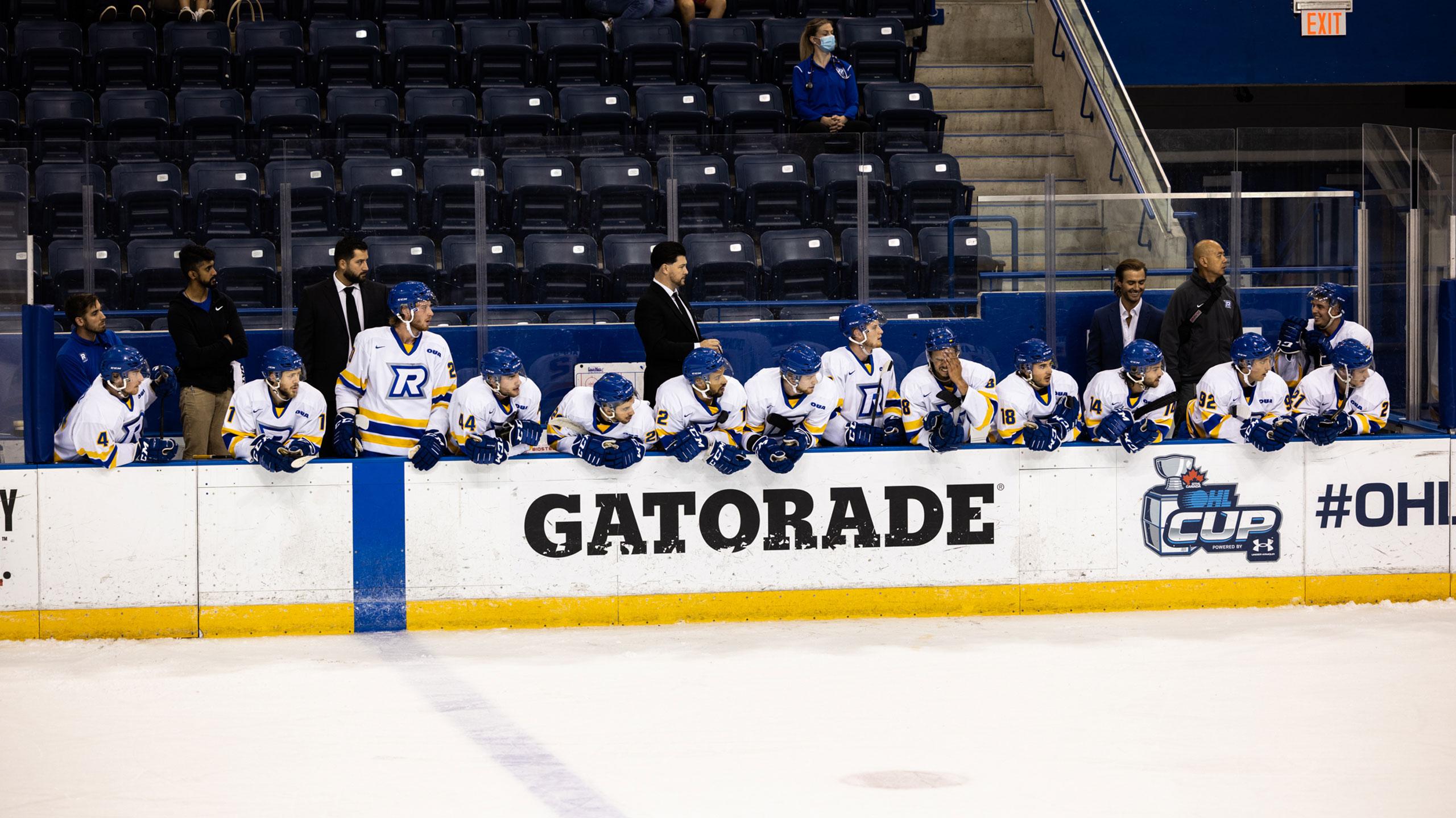The TMU men's hockey team on the bench in white jerseys
