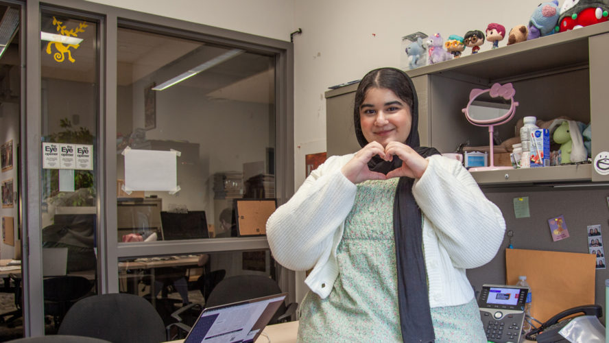 Abeer Khan sitting at her desk making a heart with her hands.