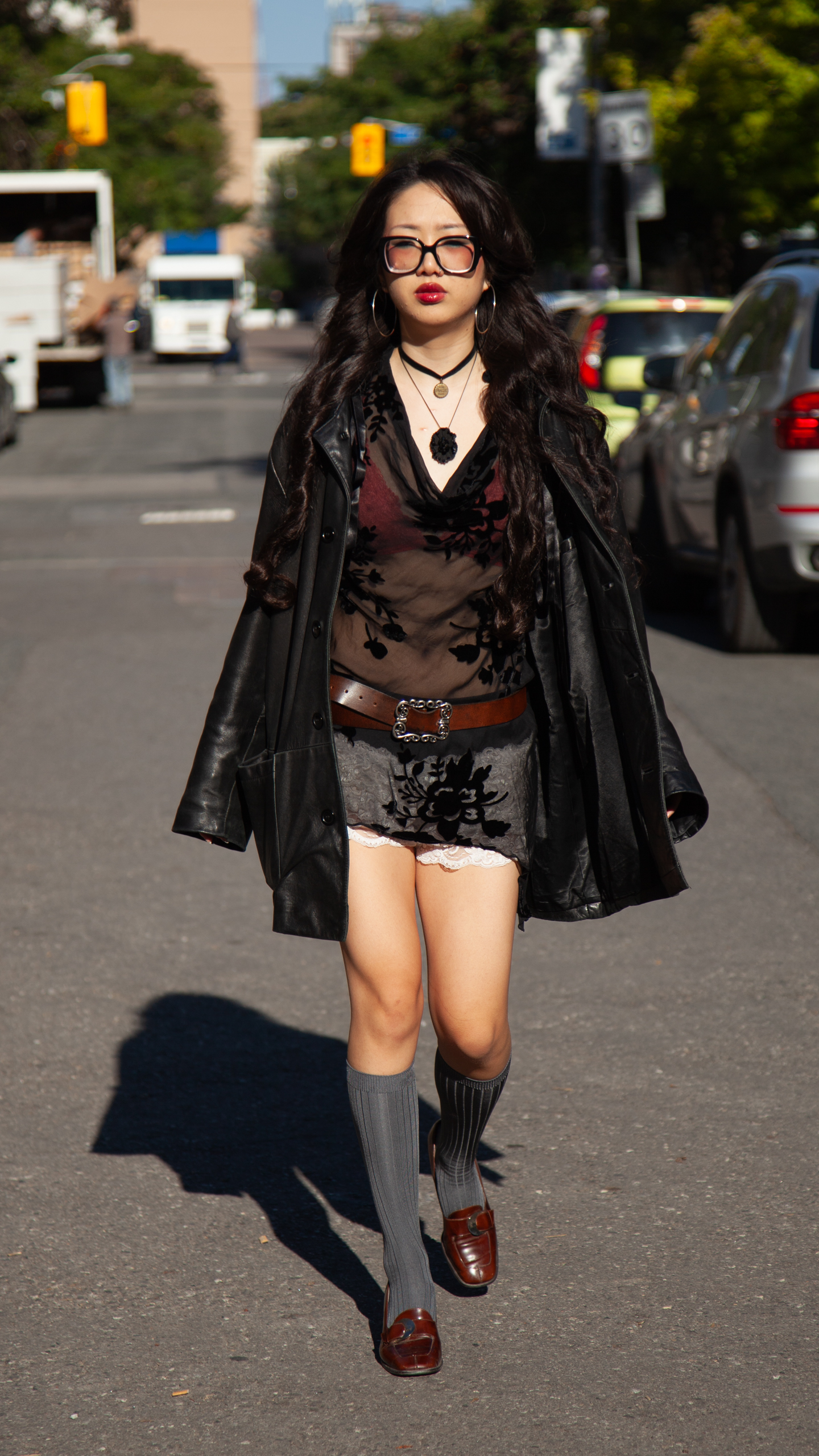 Model walking through campus wears leather jacket with sheer dress over bloomer shorts