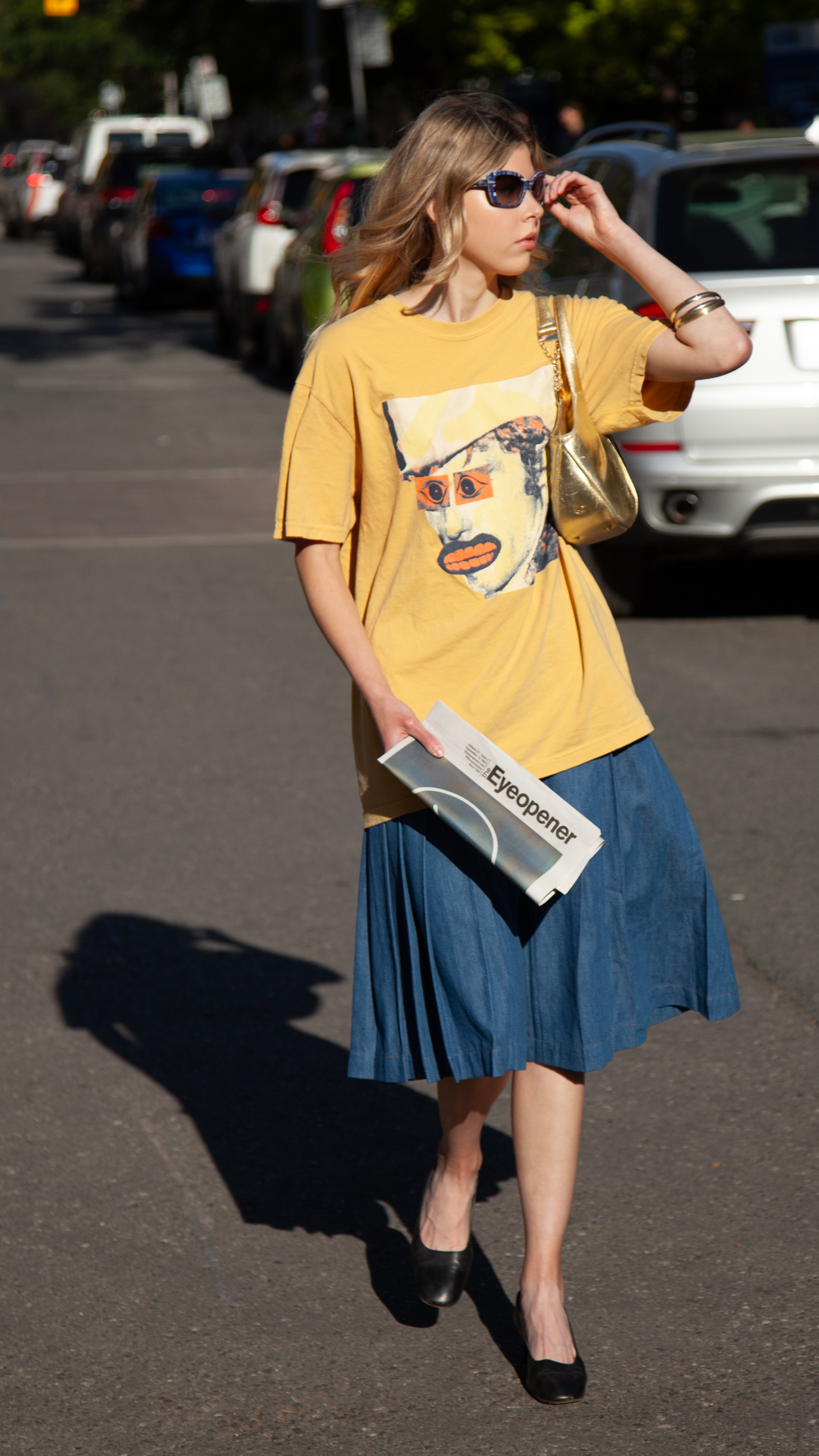 Model walking through campus wears yellow band tee and a denim circle skirt with a gold coloured handbag