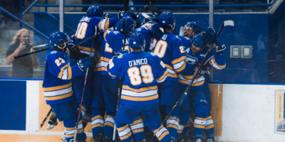 The TMU Bold men's hockey team huddle and celebrate an overtime winning goal