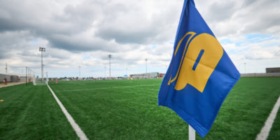 A TMU Bold corner flag in front of an empty soccer pitch