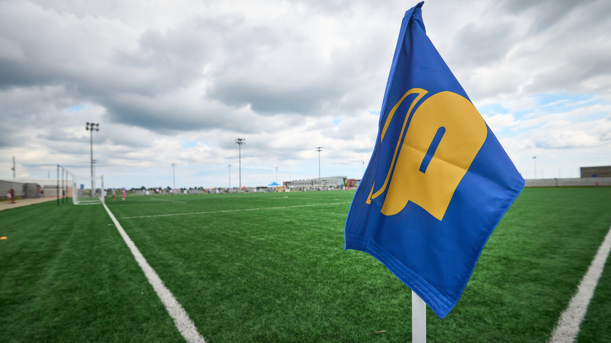 A TMU Bold corner flag in front of an empty soccer pitch